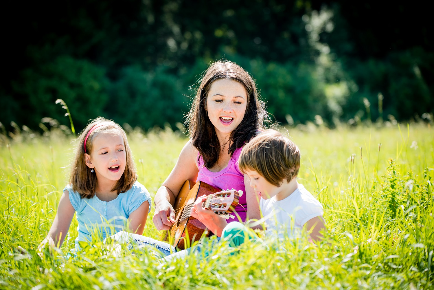 Mother playing guitar in nature to children